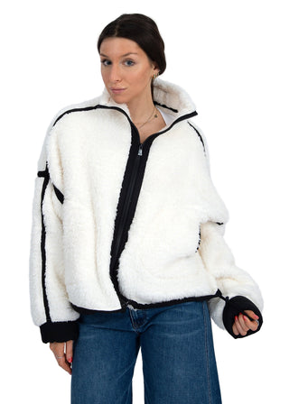 Woman wearing a white fleece jacket with black trim on a plain background