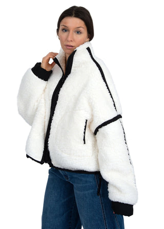 Woman wearing a white fleece jacket with black trim on a plain background