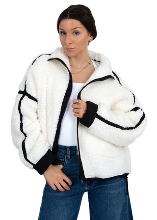 Woman wearing a white fur jacket with black trim on a plain background