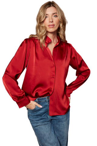 Woman wearing a red satin blouse and blue jeans against a brown background