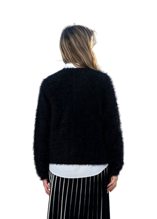 Person wearing a black sweater and striped skirt standing against a white wall with a scenic view.