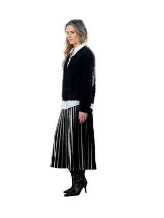 Woman in black sweater and striped skirt standing against a white wall with ocean view