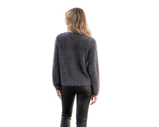 Person wearing a dark gray sweater and black pants walking on a cobblestone street.