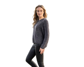 Woman wearing a gray sweater and black pants standing on a cobblestone street.