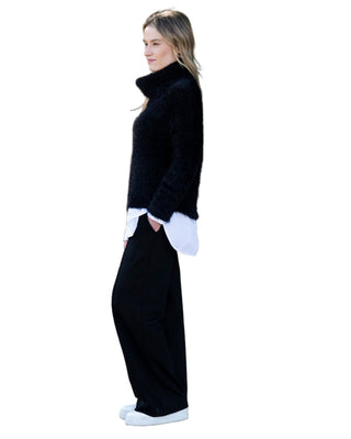 Woman wearing a black turtleneck, white shirt, black pants, and white sneakers on a cobblestone path.