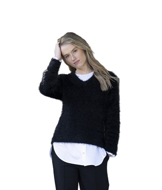 Woman wearing a black sweater over a white shirt with a blurred wooden door background
