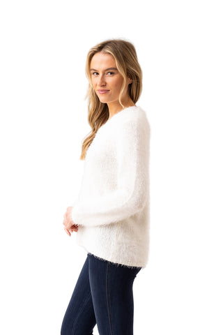 Woman wearing a white sweater and dark pants on a plain background