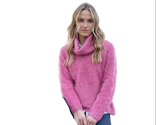 Woman wearing a pink sweater sitting on a wooden railing with a scenic background
