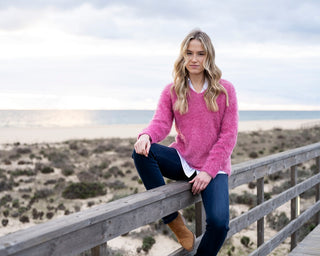Woman in a pink sweater sitting on a wooden railing with a beach in the background