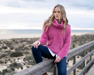 Woman in a pink sweater sitting on a wooden railing with a beach background