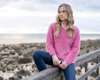 Woman wearing a pink sweater sitting on a wooden railing with a scenic background