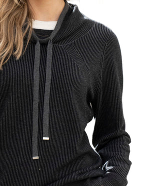 Close-up of a person wearing a dark ribbed sweater with a blurred background