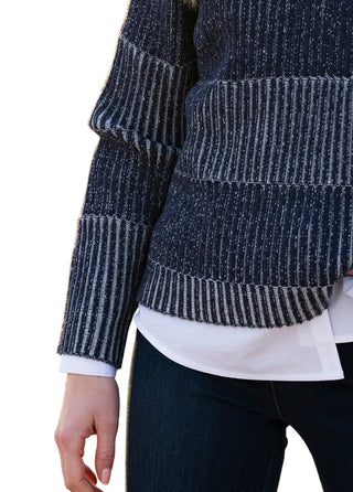Person wearing a dark gray and white striped sweater over a white shirt on a blurred background