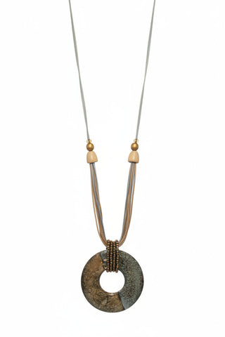A long statement necklace displayed on a black torso mannequin. The necklace has a large circular stone pendant with a central hole, accented by small metallic beads and light wood beads on a multi-strand cord.
