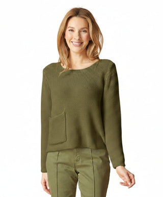 Woman wearing a cream sweater and green pants against a beige background