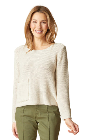 Woman wearing a cream sweater and green pants against a beige background