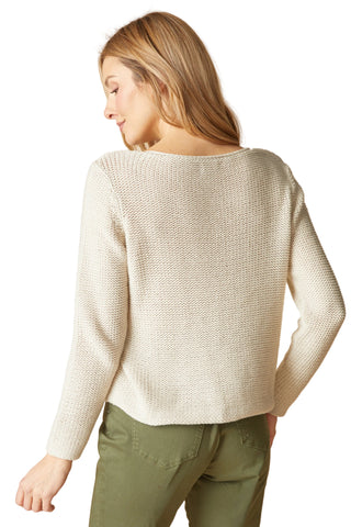 Woman wearing a beige sweater and green pants against a beige background