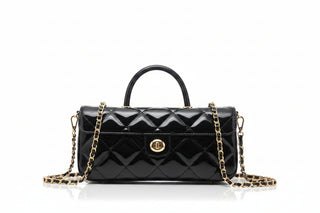 A black patent leather quilted handbag with a top handle, gold-tone chain strap, and a round gold-tone front clasp, displayed on a black metal stand.