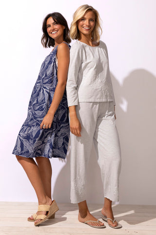 Two women standing side by side, one in a blue patterned dress and the other in a white outfit, on a plain background.