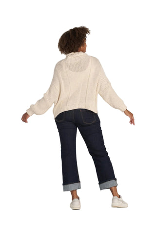 A model shown from the back wearing a cream-colored textured knit sweater, dark blue cropped jeans with rolled cuffs, and white sneakers, set against a solid light gray background.