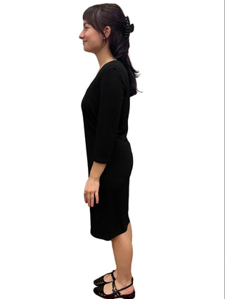 Woman wearing a black dress standing in a fitting room.