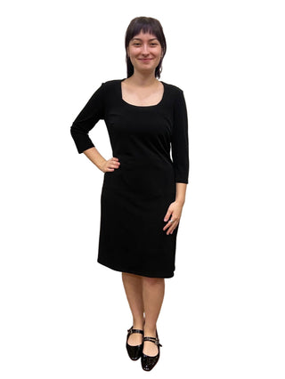 Woman wearing a black dress standing in front of a mirror.