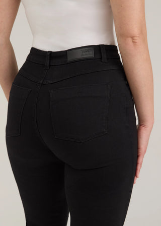 Rear view of a person wearing black high-waisted skinny jeans with a white top, showing the back pockets and waistband.
