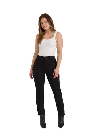 A woman modeling black slim-fit jeans with a white tank top and black pointed-toe boots, standing against a light gray studio background.