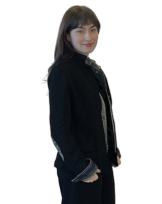 Person wearing a black coat with patterned cuffs against a plain background