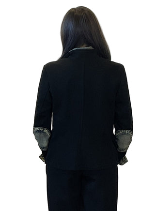 Person wearing a black suit with patterned cuffs against a plain background