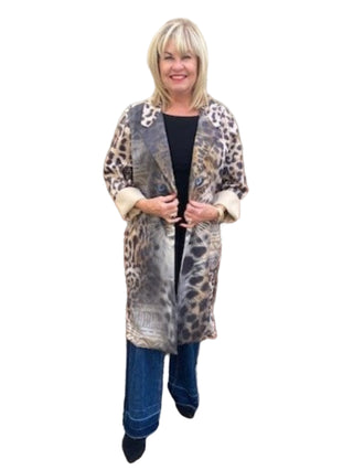 Woman wearing a long, patterned coat standing in front of a brick wall.