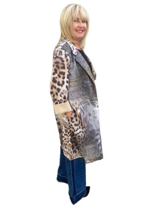 Woman wearing a leopard print cardigan, patterned dress, and blue jeans standing against a brick wall.