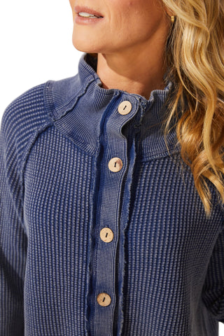 Close-up of a person wearing a blue textured shirt with wooden buttons.