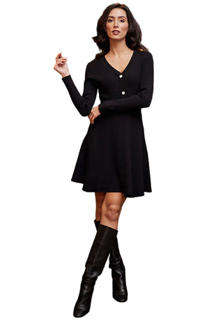 Woman in a black dress and knee-high boots standing in an indoor setting with a green couch and decorative wall.