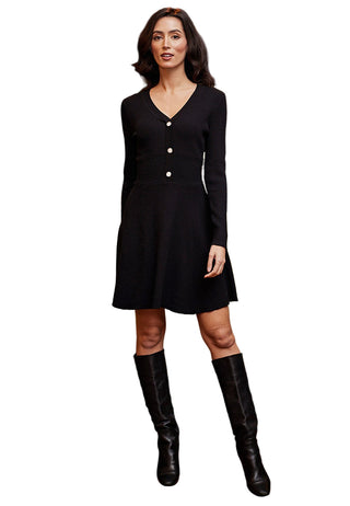 Woman in a black dress and knee-high boots standing in a room with a green couch and decorative pillows.