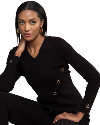 Woman wearing a black outfit with gold buttons against a wooden background