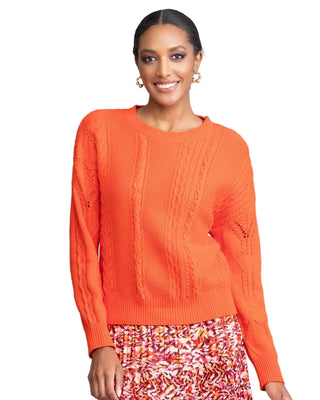 Woman wearing an orange sweater with a patterned skirt on a plain background