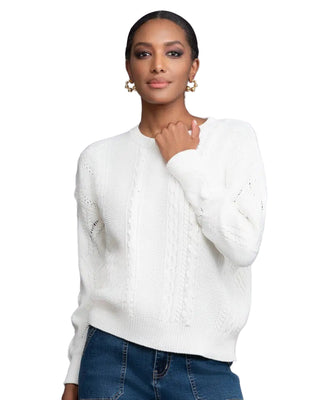 Woman wearing a white sweater and blue jeans against a gray background