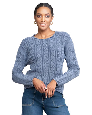 Woman wearing a blue cable knit sweater against a plain background