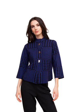 A woman modeling a navy blue and black patterned jacket with three-quarter sleeves and a high mock neck, paired with black trousers, against a solid beige background.