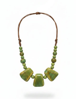 A handmade statement necklace with three large, polished olive-green ceramic beads suspended on a brown cord, displayed on a black mannequin bust.