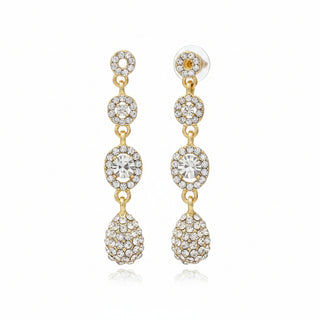 Gold and crystal drop earrings on a textured brown surface