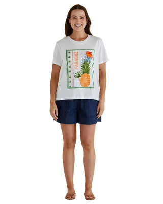 Woman wearing a white t-shirt with a pineapple graphic and denim shorts on a beige background