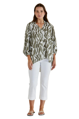 Woman wearing a green patterned blouse and white pants against a beige background