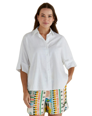 Woman wearing a white shirt and colorful patterned shorts on a beige background