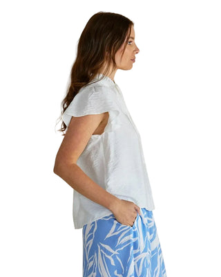 Woman wearing a white top and blue floral pants against a beige background