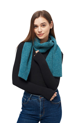 Woman wearing a teal scarf, black sweater, and blue jeans on a light gray background