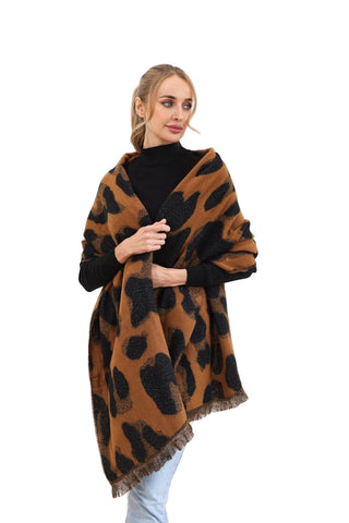 Woman wearing a leopard print poncho against a white decorative wall.