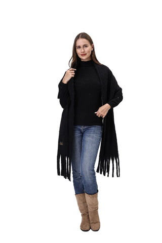 Woman wearing a black fringe coat, black turtleneck, blue jeans, and brown boots on a white background