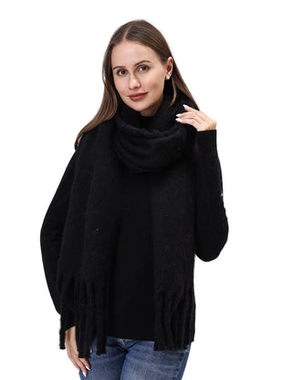 Woman wearing a black turtleneck sweater with fringe details on a light gray background